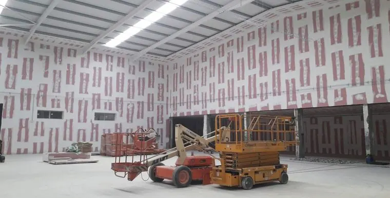 Pavilhão industrial durante a aplicação de proteção passiva contra incêndio, com plataformas elevatórias