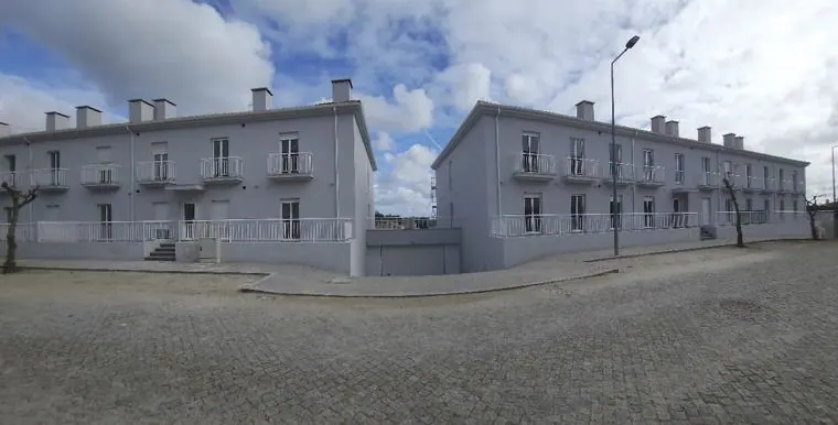 Dois edifícios habitacionais brancos com praça calcetada à frente