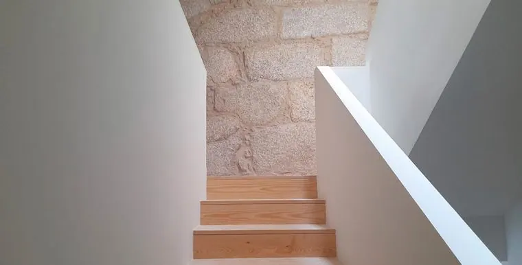 Escada em degraus de madeira encostada a parede de granito