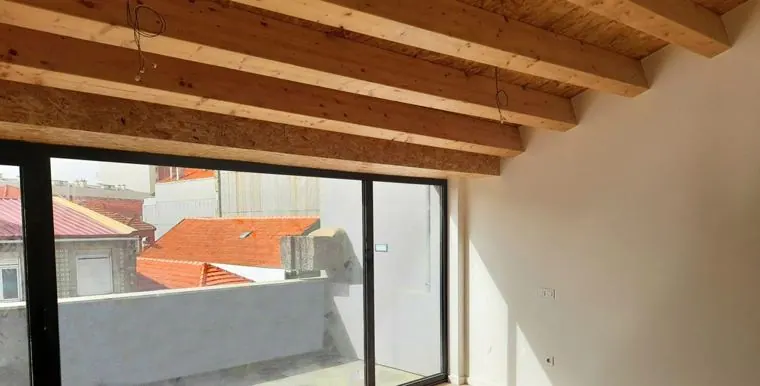 Sala em águas-furtadas com vigas de madeira e janela de canto sobre os telhados