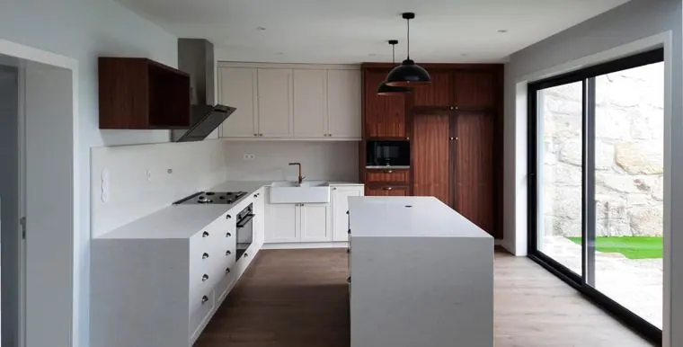 Cozinha com ilha branca, armários de madeira escura e porta para o jardim