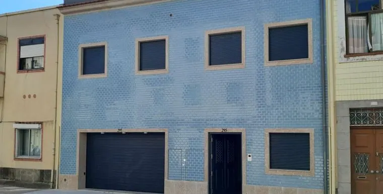 Fachada de moradia revestida a azulejo azul com portão de garagem