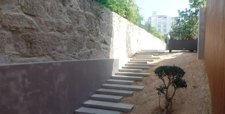 Escadaria exterior em pedra entre muros de granito e jardim