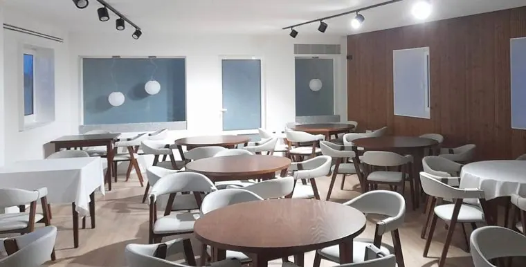 Espaço de restauração reabilitado com mesas redondas e parede em madeira